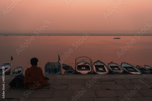 Sadu meditating in orange clothes during dawn on sacred river Ganges in Varanasi, India