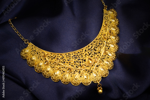 Indian traditional gold jewellery of a Hindu Married woman called as ganthan or choker, necklace on blue silk background. Creative jewellery product photography.