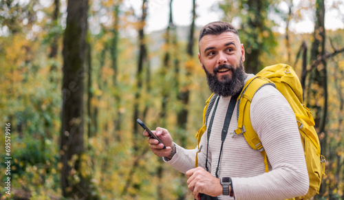 During his forest hike, a bearded young man consults his smartphone for directions.