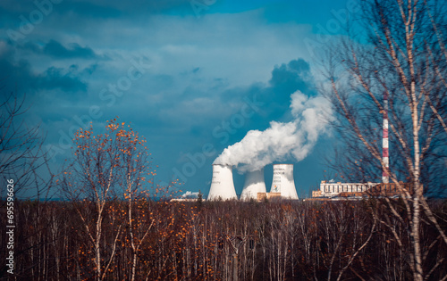 Nuclear power plant cooling towers concept photo. Big chimneys. Forest with partly cloudy sky in Polish province.