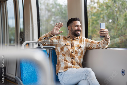 handsome latin man makes a video call with his smartphone while riding the train waving