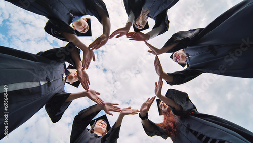 College graduates make a circle of their hands.