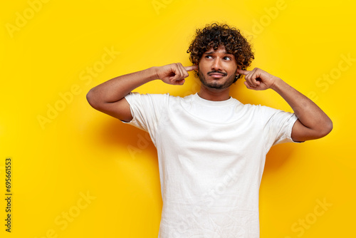 young indian guy avoids and ignores noise over yellow isolated background
