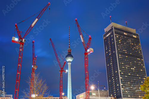 The famous Television Tower of Berlin at night with a skyscraper and four red construction cranes
