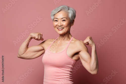 An older woman showcasing her strength by flexing her muscles on a vibrant pink background. Suitable for fitness and wellness-related designs
