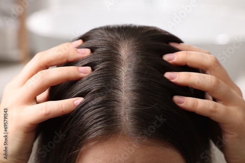 Woman examining her hair and scalp on blurred background, closeup