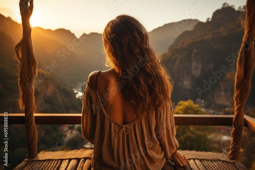 Picture from behind of a woman sitting on a wooden balcony The sun was setting on the mountains and had a beautiful warm orange glow