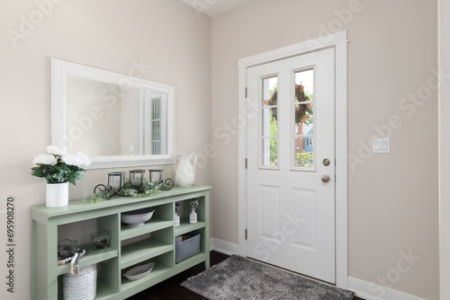 A cozy entryway with brown walls, a green console table with decorations, and a white front door.