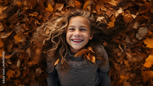 A young girl with long hair smiling in a pile of freshly raked leaves. The season is autumn.