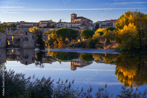 View of the city of Zamora and watermills and the San Pedro Church in the background in autmn at sunset reflected in the Duero river. Spain
