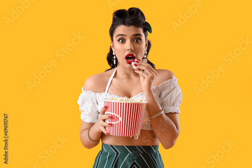 Scared young pin-up woman with popcorn on yellow background