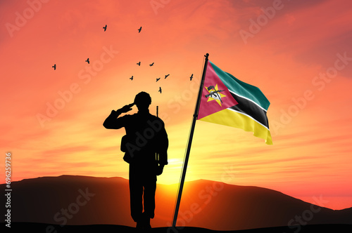 Silhouette of a soldier with the Mozambique flag stands against the background of a sunset or sunrise. Concept of national holidays. Commemoration Day.