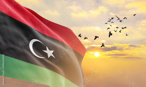 Waving flag of Libya against the background of a sunset or sunrise. Libya flag for Independence Day. The symbol of the state on wavy fabric.