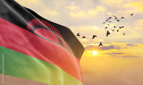 Waving flag of Malawi against the background of a sunset or sunrise. Malawi flag for Independence Day. The symbol of the state on wavy fabric.