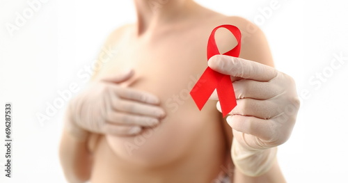 Female hand in gloves holding red ribbon cancer symbol breast closeup on doctor mammology clinic reception. Mammary glands test biopsy implant silicone insert tumor human concept