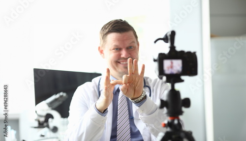 Focus on male hands of handsome doctor showing funny jokes with gestures by hands. Smiling blogger recording popular video content to camera. Blogging concept