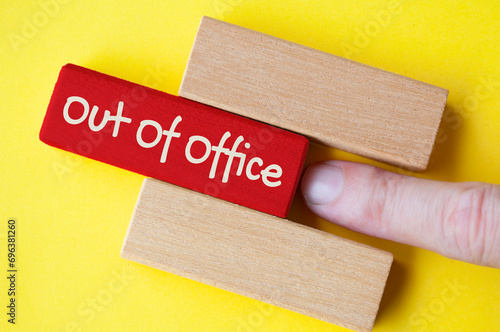 Finger pushing out red wooden block with out of office text on yellow cover background