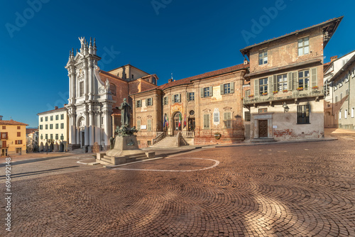Bra, Cuneo, Italy - The town hall and parish church Sant' Andrea Apostolo in Piazza Caduti per la Liberta, Coblestone with the statue of St. Joseph Cottolengo