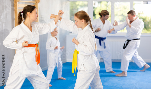 Focused teen girl and woman in kimono practices combat technique of punching and blocking at family martial arts class