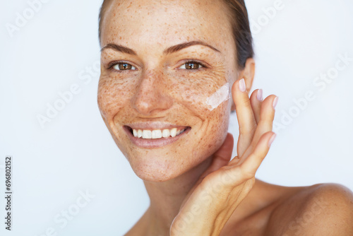 Beautiful woman with a freckles is applying a facial skincare cream and smiling. Beauty skin care, hydration and moisturising treatment