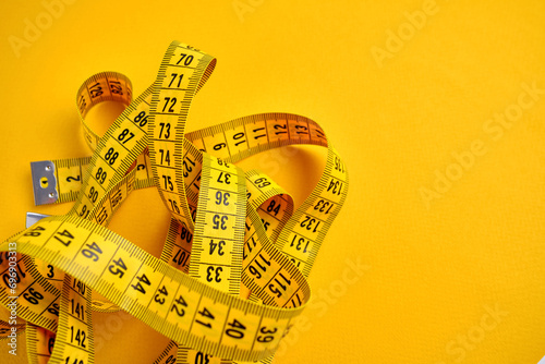 Yellow measuring tape on a yellow background. Tool for measuring length and volume. Tape for measuring in the clothing industry or the volume of the human body 