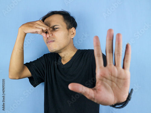 gesture handsome Asian man smelling something stinky and disgusting, intolerable smell