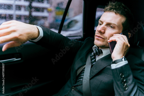 タクシーに乗ってスマホで話しながら行き先を指示する乗客の欧米人ビジネスマン 