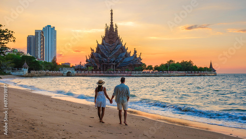 A diverse multiethnic couple of European men and Asian women visit The Sanctuary of Truth wooden temple in Pattaya Thailand at sunset