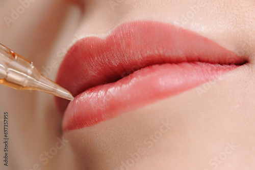 Procedure permanent makeup in beauty salon, tattoo machine with red pigment on woman lips
