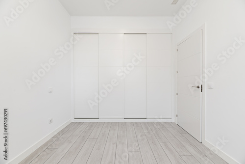 An empty room in a loft-type home with a built-in wardrobe covering the entire wall with white wooden sliding doors