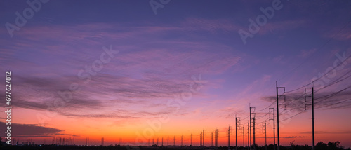 Silhouette two rows of electric poles with cable lines on curve road in countryside against colorful twilight sky background after sundown, panoramic view