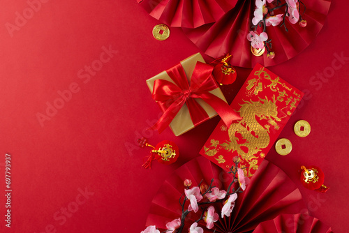 Gift suggestions for Chinese New Year festivities. Top view photo of red featuring fans, traditional envelope, gift box, sakura bloom, lucky coins on red background with promo zone
