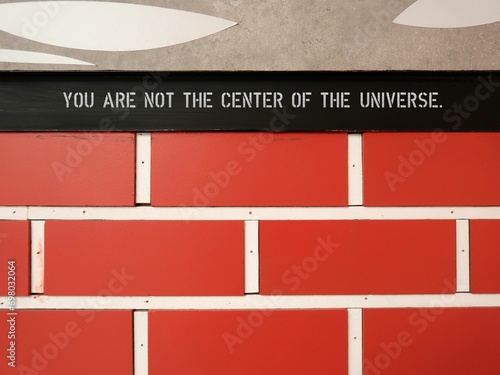 Brown brick wall with text inscription YOU ARE NOT THE CENTER OF THE UNIVERSE, to remind we are not focus of everyone attention, we are much more focus of ourselves mistakes and flaws