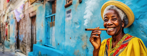 Elderly Woman Enjoying a Cigar Against a Blue Wall in Havana. Smiling Senior Lady in Yellow Dress and Straw Hat with Cigar in Cuba