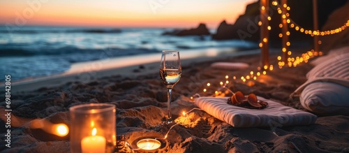 Romantic beach date by California ocean waves with candlelight, wineglass on sand, and cozy lounge garland at sunset.