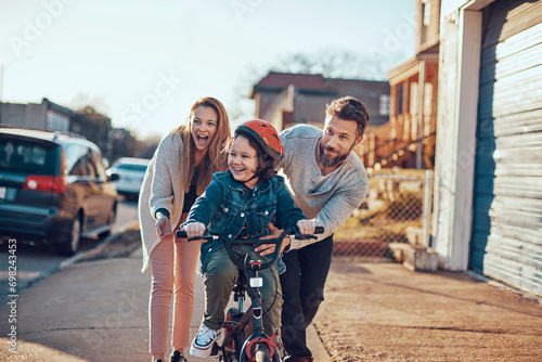 Happy young boy having first bike ride with parents outside