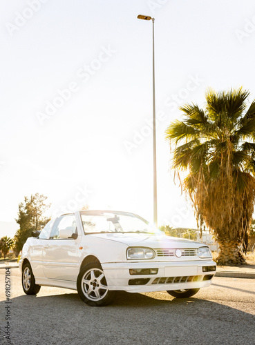 Vertical photo of a white 1996 convertible at sunset. Old car without a roof. Cabriolet convertible in coastal area. Travel with vintage cars with fabric roofs.