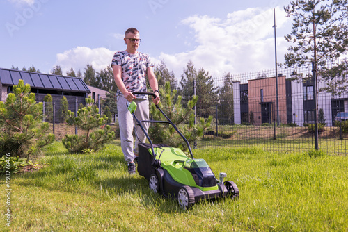 A young woman with a green lawn mower mows the lawn