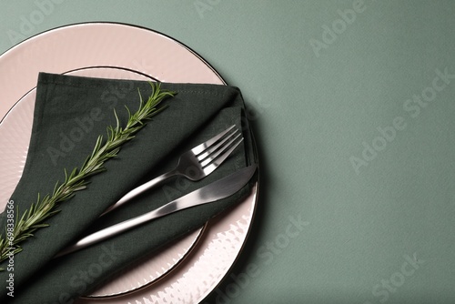 Stylish table setting. Plates, cutlery, napkin and rosemary on green background, top view with space for text