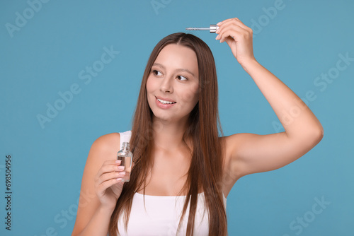 Beautiful woman applying serum onto hair on light blue background
