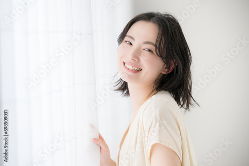 窓辺に佇む若い女性 カメラ目線の笑顔