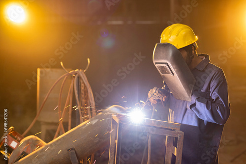 Industrial worker welding metal part at factory