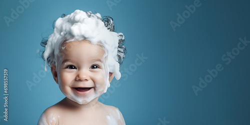 Little smiling baby boy with big soap foam on her head in her hair on a blue background. Copy space