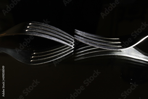 Tenedores de acero de cuatro puntas como utensilios de comida, reflejados en la superficie formando ondas y curvas abstractas, crean un original diseño culinario sobre un fondo negro