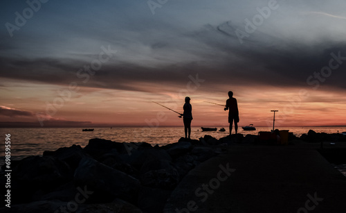 Dwoje wędkarzy dziewczyna i chłopak, sylwetki osób, zachodzące słońce nad brzegiem morza, Adiatyk, Chorwacja, Istria skalisty brzeg