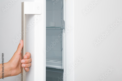 Young adult woman hand holding handle and opening or closing white freezer door. Closeup. Side view.