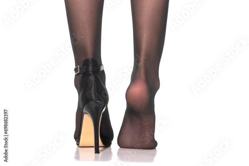 Closeup of female feet in black nylon leggings, with and without high heel shoe on white background