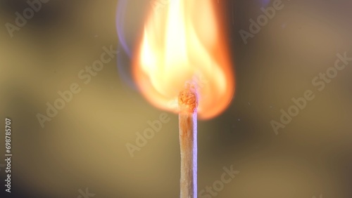 Macro shot of a burning match against a yellow studio background. The flame of the burning match illuminates the dark space. The burning match is enveloped in an orange, vibrant and dynamic flame.