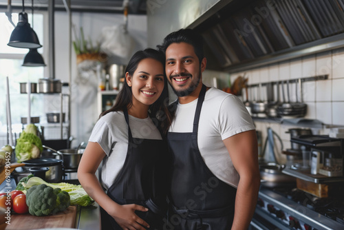 Smiling young hispanic couple posing at their restaurant kitchen 