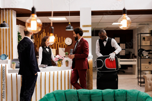 Colleagues greeted by receptionist at front desk, partners in suits arriving at luxury hotel to attend executive business meeting, travelling for work. Men on journey, conference participation.